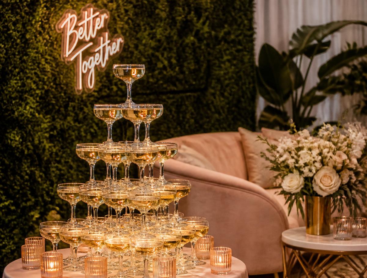 Champagne coupe tower against a greenery wall with blush lounge seating